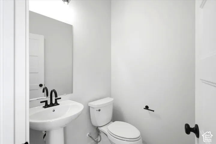 Pedestal sink with matte black faucet, wall-mounted mirror, and white toilet
