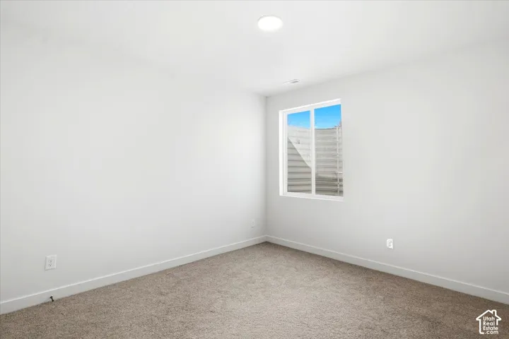 Recessed ceiling lighting, white painted walls, single window with white frame, light brown carpet, and white electrical outlets