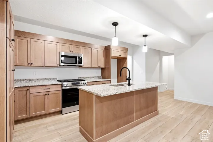 Kitchen featuring wood-finish cabinetry, stainless steel appliances, granite countertops, and a kitchen island with a matte black faucet