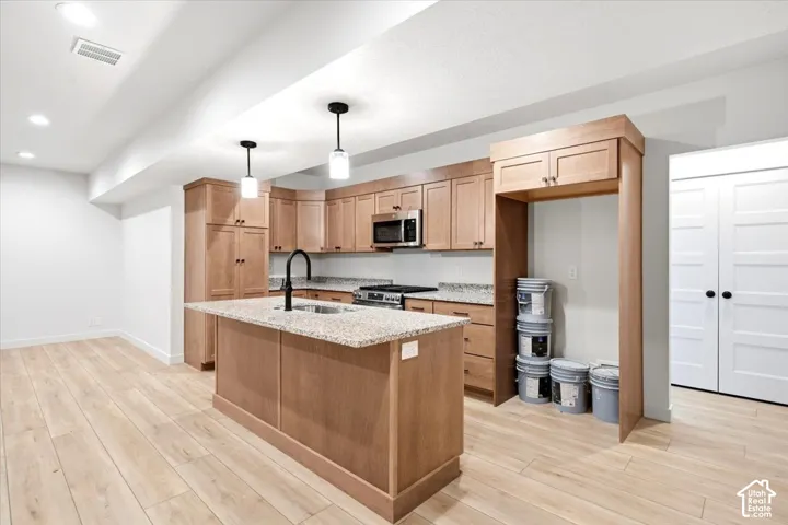 Kitchen featuring a central island with an undermount sink, pendant lighting, wood-finish cabinetry, and stainless steel appliances