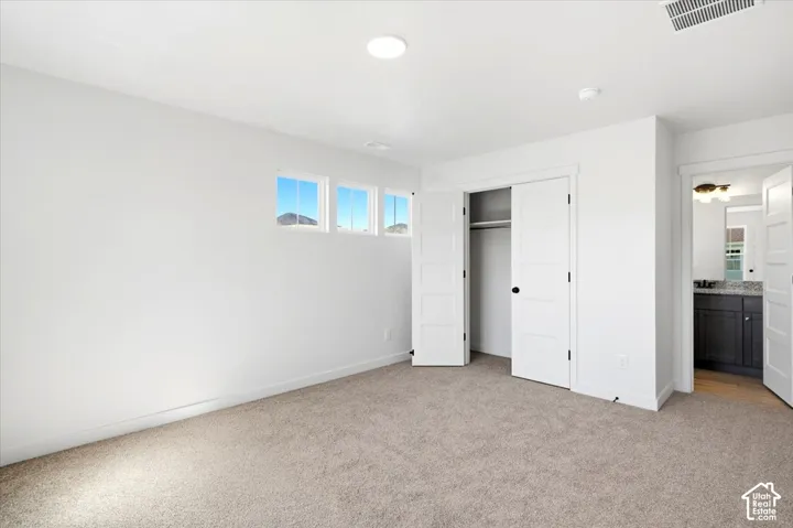 Recessed lighting, soft carpet flooring, built-in closet, transom windows, and an en-suite bathroom with a dark wood vanity and light-colored countertop