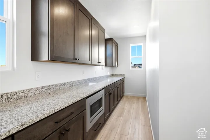 Dark wood-finish cabinetry with abundant storage, light granite countertops, an integrated stainless steel microwave, and wood-finish flooring
