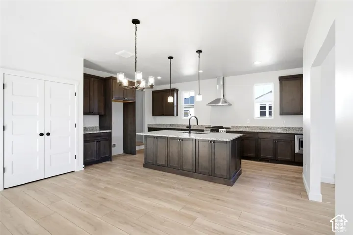 Spacious kitchen featuring dark wood cabinetry, light-toned countertops, a central island with a built-in sink, stainless steel range hood, and wood-finish flooring