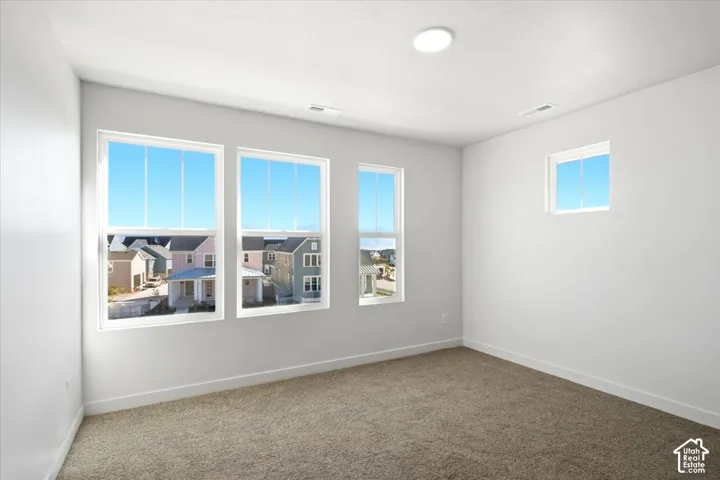 Four windows providing natural light, light-colored walls, recessed ceiling lighting, and carpet flooring