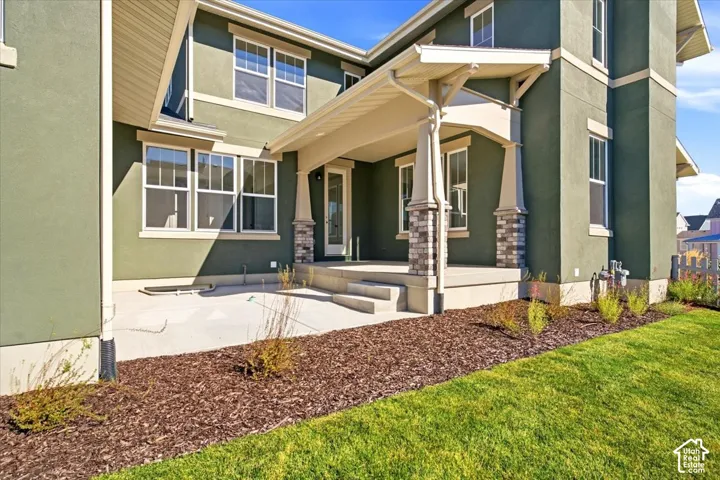 Exterior featuring a covered patio, stucco finish, stone column accents, and a manicured lawn