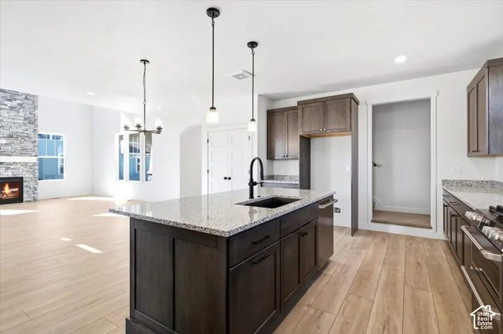 Kitchen with wood-finish flooring, granite countertops, dark wood cabinetry, and a kitchen island with a built-in sink and pendant lighting