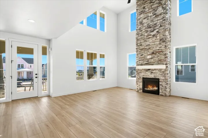 Two-story great room with a stone-clad fireplace, wood-finish flooring, high vaulted ceilings, and extensive window placement