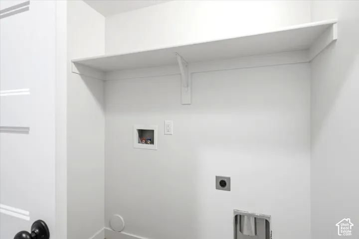 White laundry space featuring a built-in shelf, appliance hookups, and a white paneled door with matte black hardware
