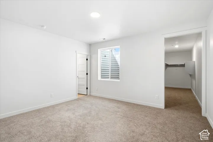 Recessed lighting, light-toned carpeting, a window with horizontal blinds, and a walk-in closet with built-in shelving