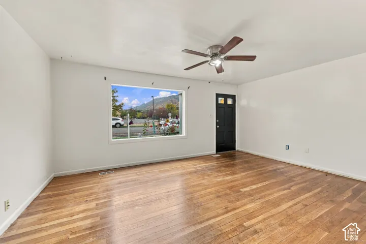 Wood-finish flooring, large picture window with mountain backdrop, and ceiling fan with integrated lighting