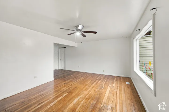Spacious room showcasing rich wood-finish flooring, white walls, and abundant natural light from large windows