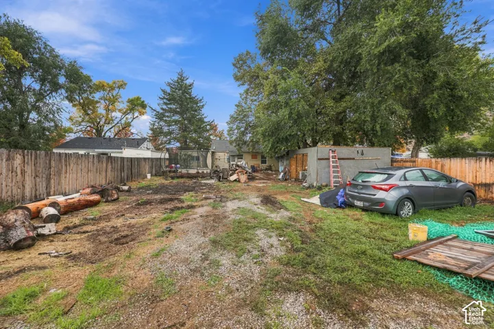 Large fenced backyard featuring perimeter wood fencing, mature trees, and a detached structure