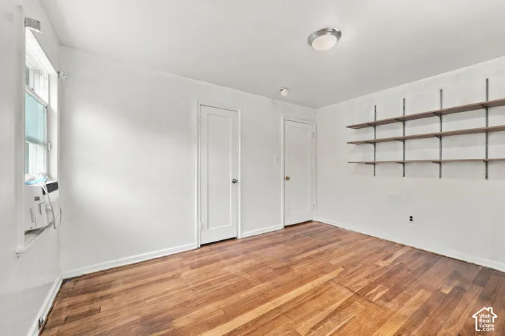 Room featuring wood-finish flooring, built-in wall-mounted shelving, flush-mount lighting, and two interior doors