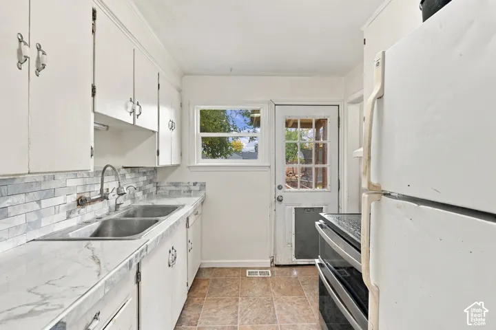 Kitchen featuring white cabinetry, stone-finish countertops, tile backsplash, stainless steel double-basin sink, and a multi-lite exterior door