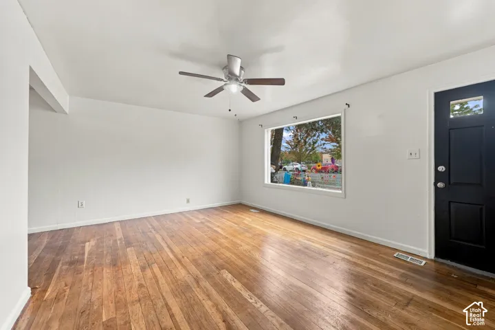 Interior space featuring wood-finish flooring, a large picture window, a ceiling-mounted light fixture with fan, and a black paneled door with glass inlay