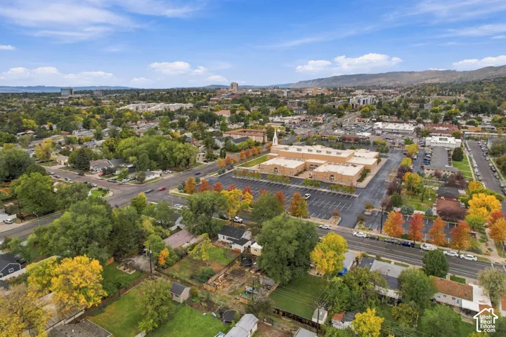 Aerial perspective of the property surroundings featuring a residential neighborhood, established mature trees, mountain backdrop, and paved street access