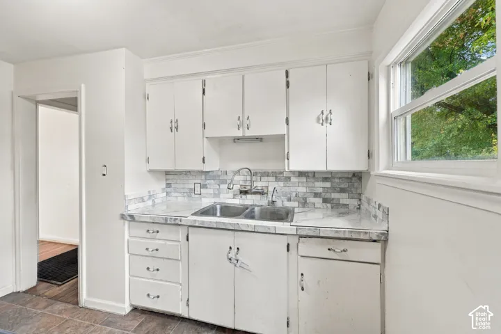 Kitchen featuring white cabinetry, stone-finish countertops, brick-style tile backsplash, dual-basin stainless steel sink with gooseneck faucet, and a dual-pane window