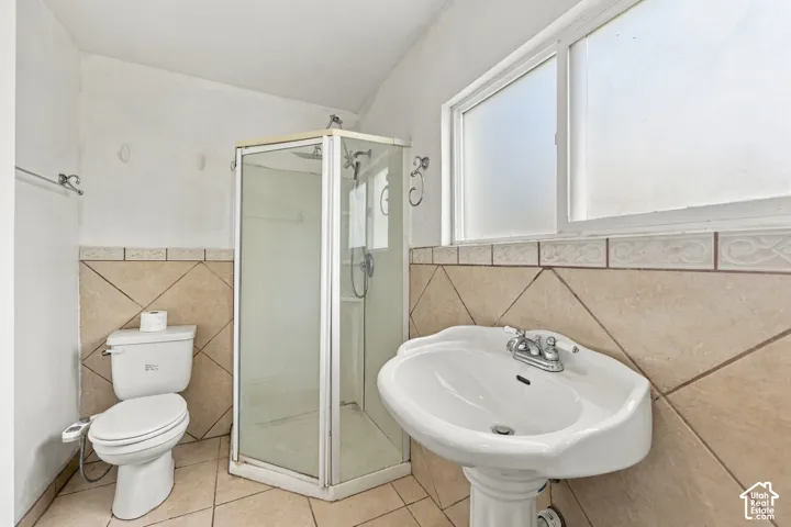 Bathroom featuring a corner glass-enclosed shower, pedestal sink with dual-handle faucet, and diagonal ceramic tile wainscoting with decorative border trim