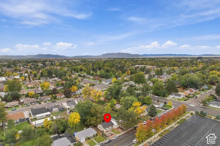 Aerial perspective of a detached residential property featuring a pitched roofline, mature trees, a fenced yard, and a mountain backdrop