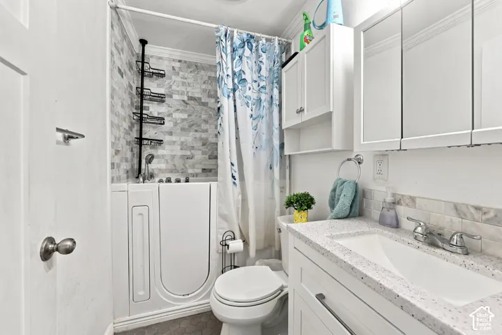 Bathroom featuring a walk-in tub with tile surround, vanity with stone-composite countertop, undermount sink, and mirrored medicine cabinet