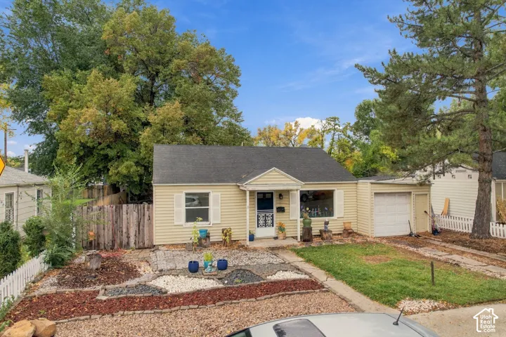 Exterior featuring light-toned horizontal siding, gable roofline, attached garage, decorative window shutters, and low-maintenance landscaping with rock beds