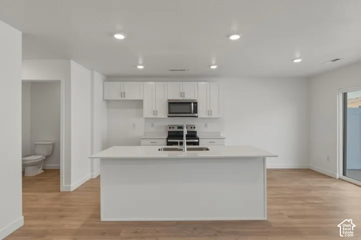 Kitchen with white cabinetry, stainless steel appliances, a center island with an undermount sink, recessed lighting, and wood-finish flooring
