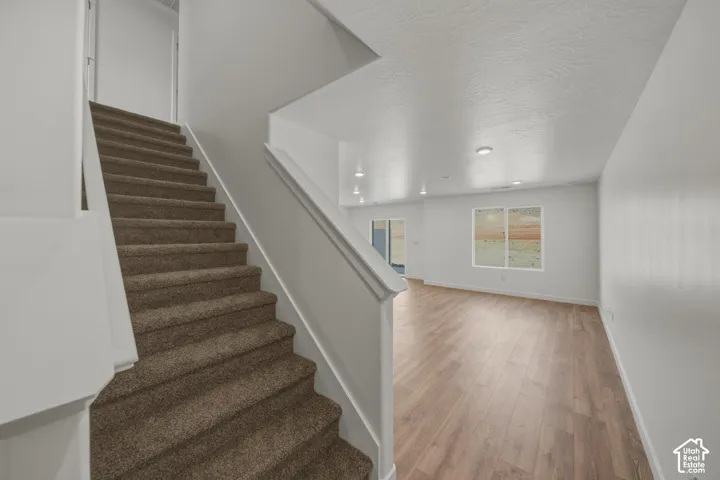 Carpeted staircase with white risers, wood-finish flooring, recessed lighting, and white walls