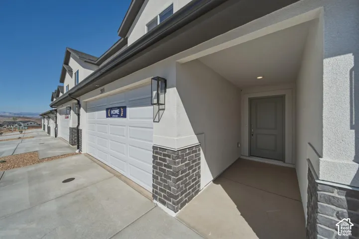 White garage door with an exterior wall sconce, textured facade, and stone veneer accents
