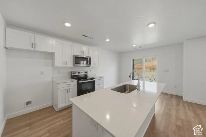 Kitchen featuring white cabinetry, light-toned countertops, stainless steel appliances, and wood-finish flooring