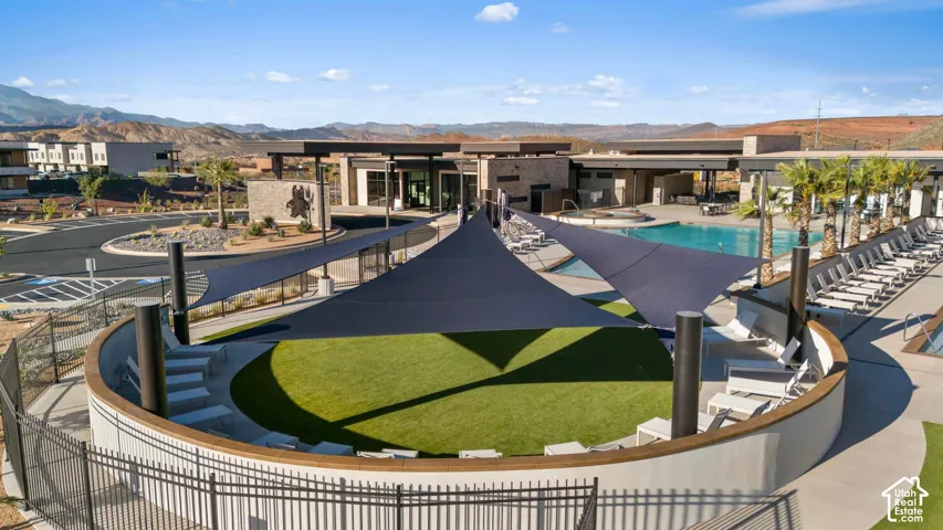 Expansive outdoor recreation area featuring a swimming pool, multiple shaded lounging areas, and terraced seating surrounding an artificial turf lawn
