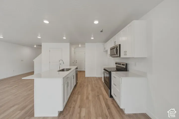 White cabinetry, stainless steel appliances, wood-finish flooring, recessed lighting, and a kitchen island with sink