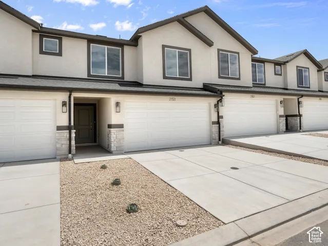 Stucco exterior with dark trim accents, stone veneer columns, multiple attached garages, concrete driveways, and low-maintenance gravel landscaping