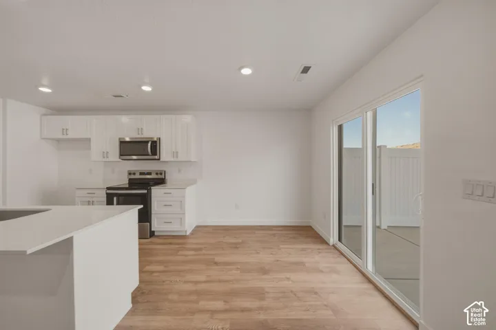 Kitchen featuring white cabinetry, stainless steel appliances, a white island with an integrated countertop, wood-finish flooring, and recessed lighting