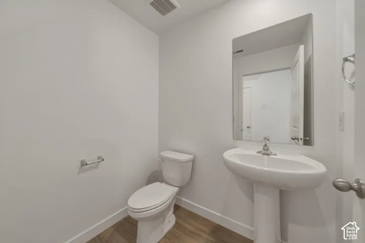Pedestal sink with chrome faucet, wall-mounted mirror, and wood-finish flooring