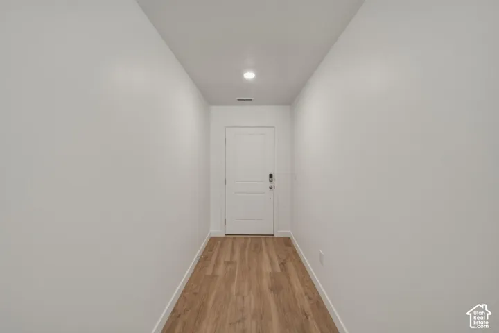 Wood-finish flooring, white walls, recessed lighting, and a white interior door