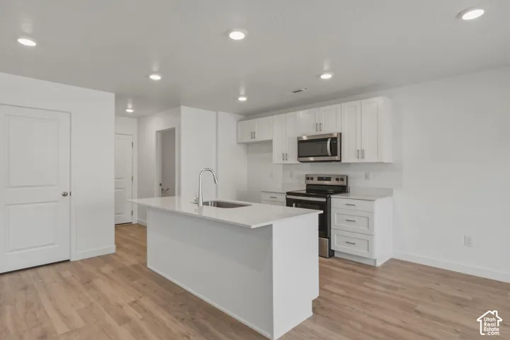 Kitchen featuring white cabinetry, stainless steel appliances, a center island with sink, recessed lighting, and wood-finish flooring