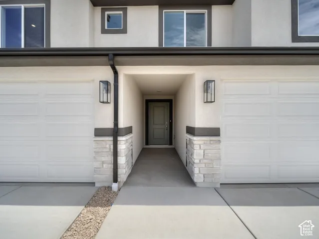 Stucco exterior with stone accent detailing, two panel garage doors, and exterior wall sconces
