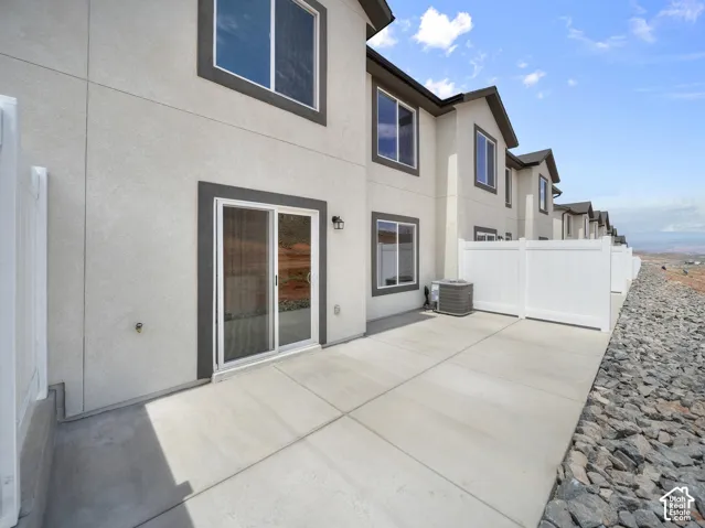 Rear exterior featuring stucco siding, sliding glass door, concrete patio, and white privacy fencing