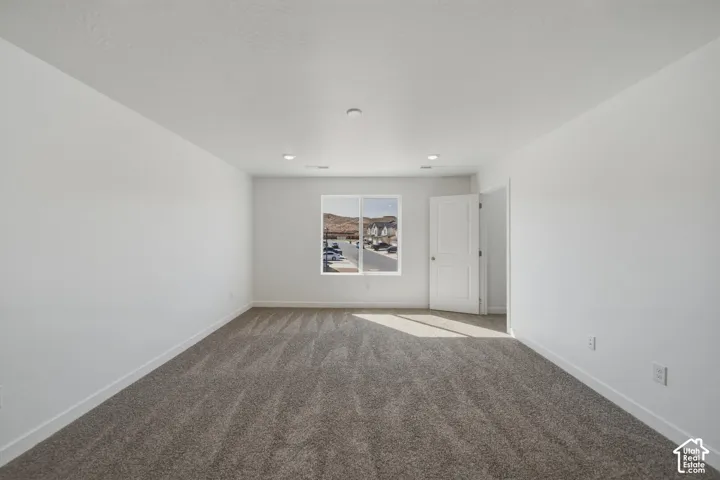 Spacious room featuring neutral carpeting, a white interior door, and recessed ceiling lighting
