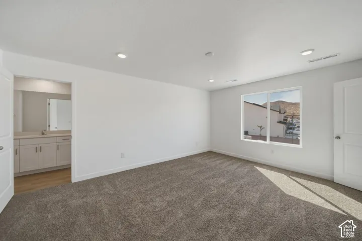 Spacious room featuring carpeting, recessed lighting, a large window, a flat-panel door, and an entryway to a vanity area with light wood-finish flooring