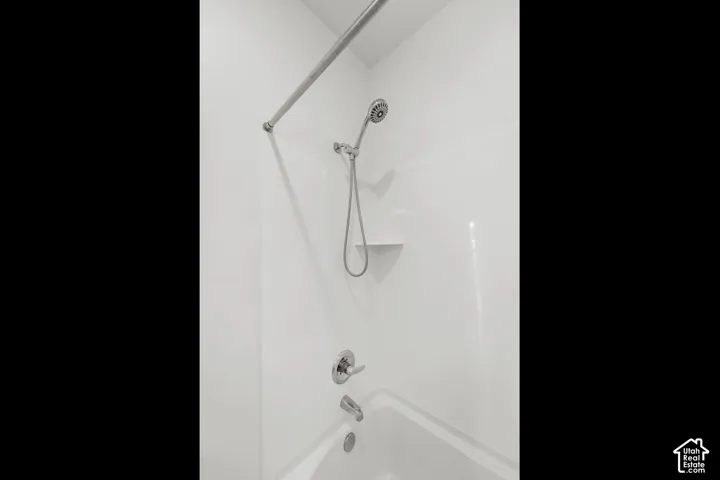 Bathtub with white surround, chrome showerhead, and integrated shelving