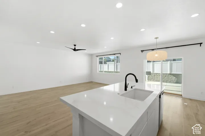 Spacious open-concept area featuring wood-finish flooring, recessed lighting, a modern ceiling fan, and a kitchen island with an integrated sink and gooseneck faucet
