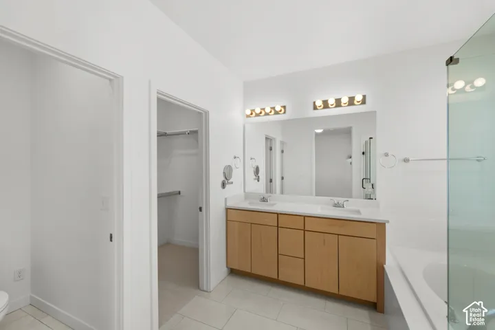 Dual vanity with integrated sinks, light wood-finish cabinetry, a large mirror, and wall-mounted lighting fixtures