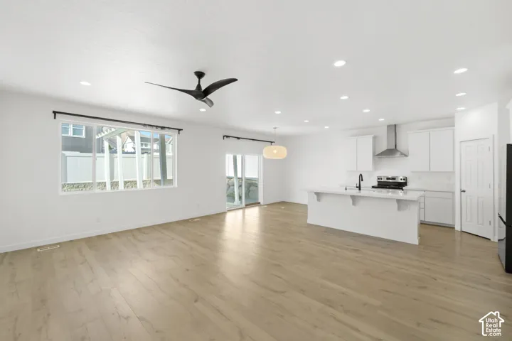 Open-concept living area featuring wood-finish flooring, recessed lighting, a modern ceiling fan, and a kitchen with white cabinetry and a central island