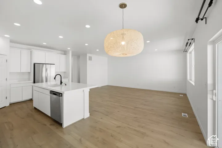 Open-concept living space with wood-finish flooring, recessed lighting, and a white kitchen featuring a large island with a quartz-style countertop and stainless steel appliances