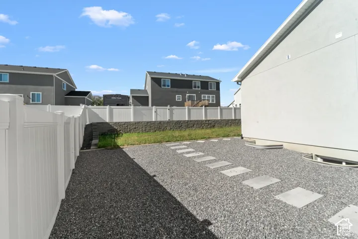 Gravel hardscaping with concrete stepping stones, white vinyl fencing, and a stucco exterior