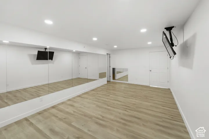 Wide plank wood-finish flooring, recessed lighting, and expansive wall-mounted mirrors
