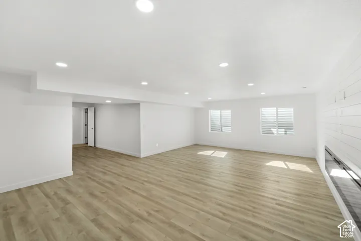 Expansive open-concept room featuring wood-finish flooring, recessed lighting, two windows with plantation shutters, and a shiplap accent wall with a built-in electric fireplace
