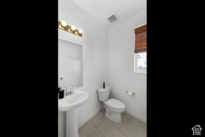 Pedestal sink, wall-mounted mirror, vanity lighting fixture, toilet, and window with a woven shade