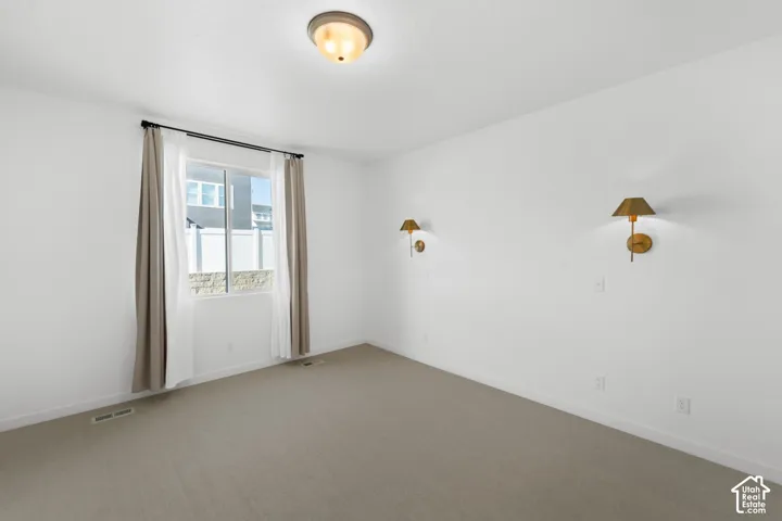 Neutral tone wall paint, carpeted flooring, window with a black curtain rod, two wall-mounted sconces, and a ceiling-mounted light fixture